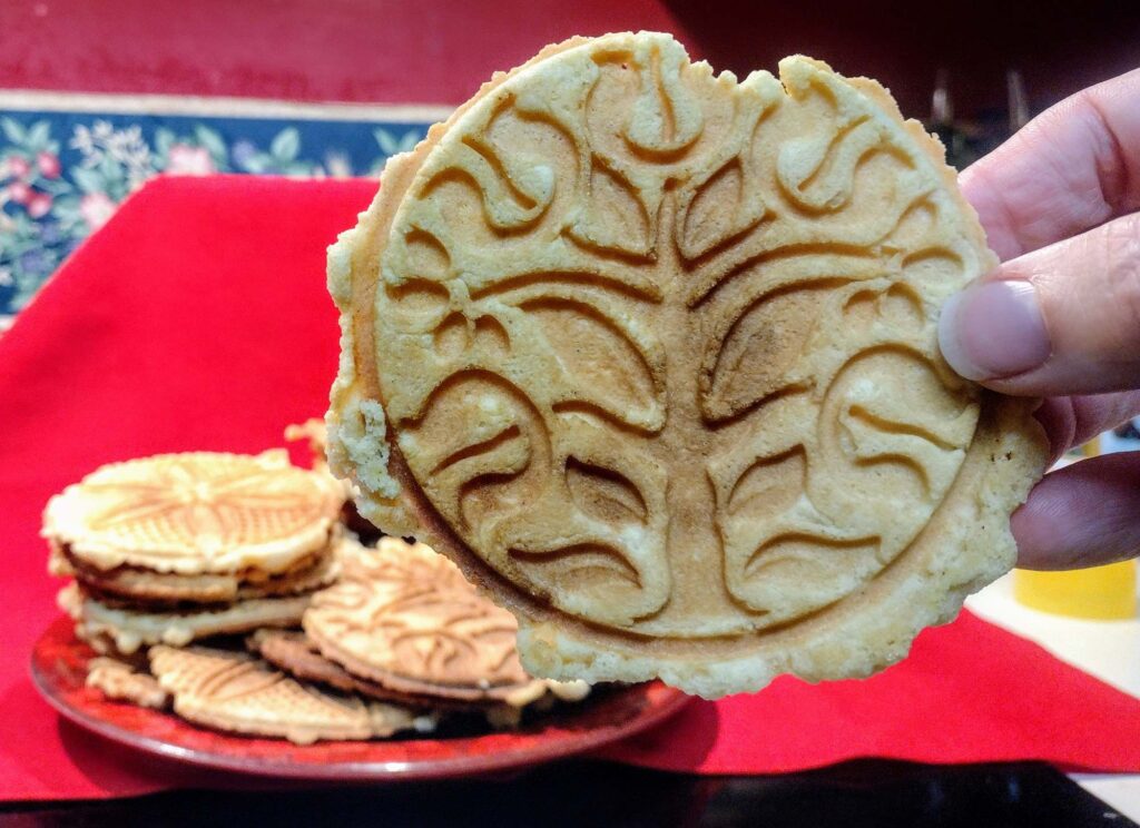 Single pizzelle cookie held up in front of stack.