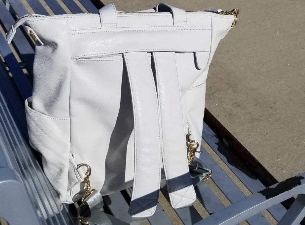 Caroline bag features backpack straps that can be stored. Bag is sitting on a bench.