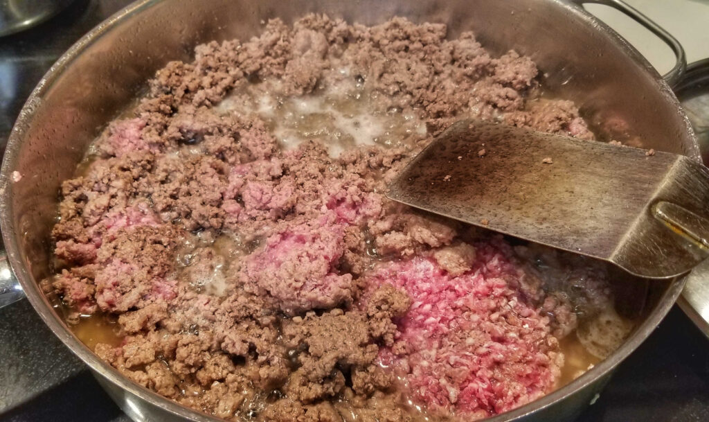 Browning ground beef in large skillet with spatula for stirring.