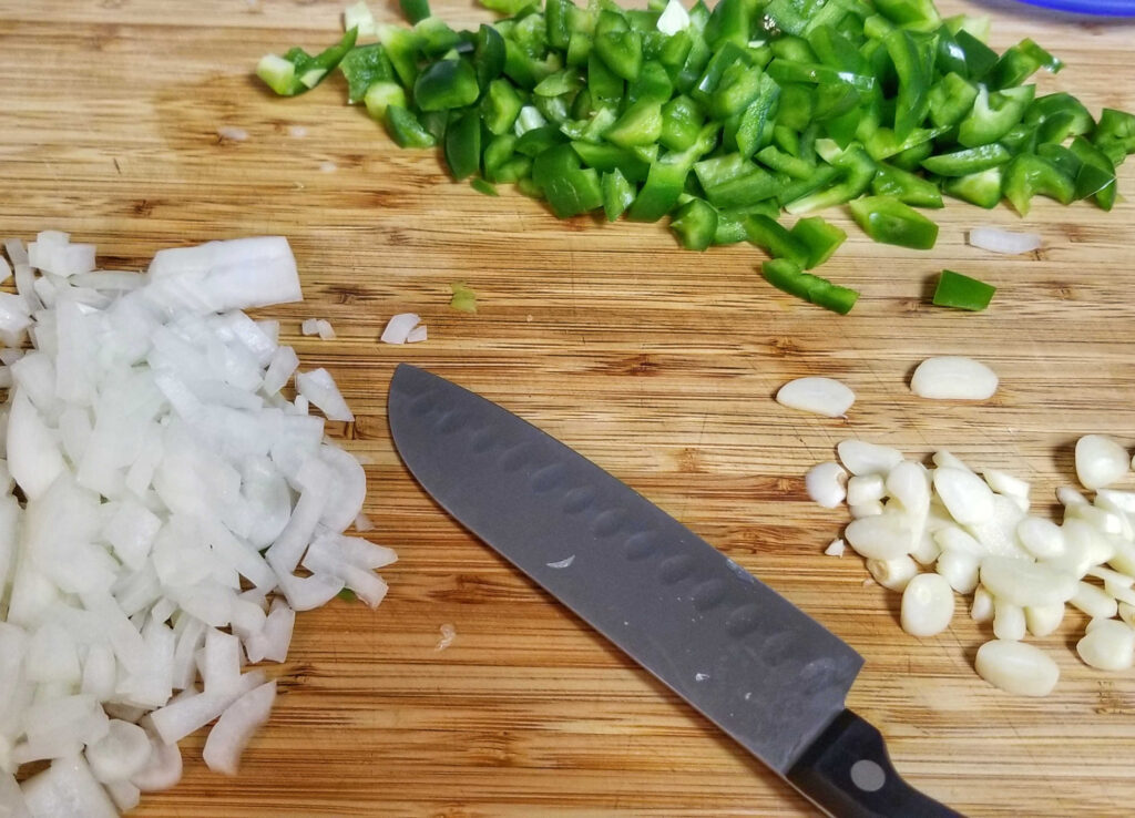 Diced onions, green pepper and garlic on cutting board with small chefs knife.