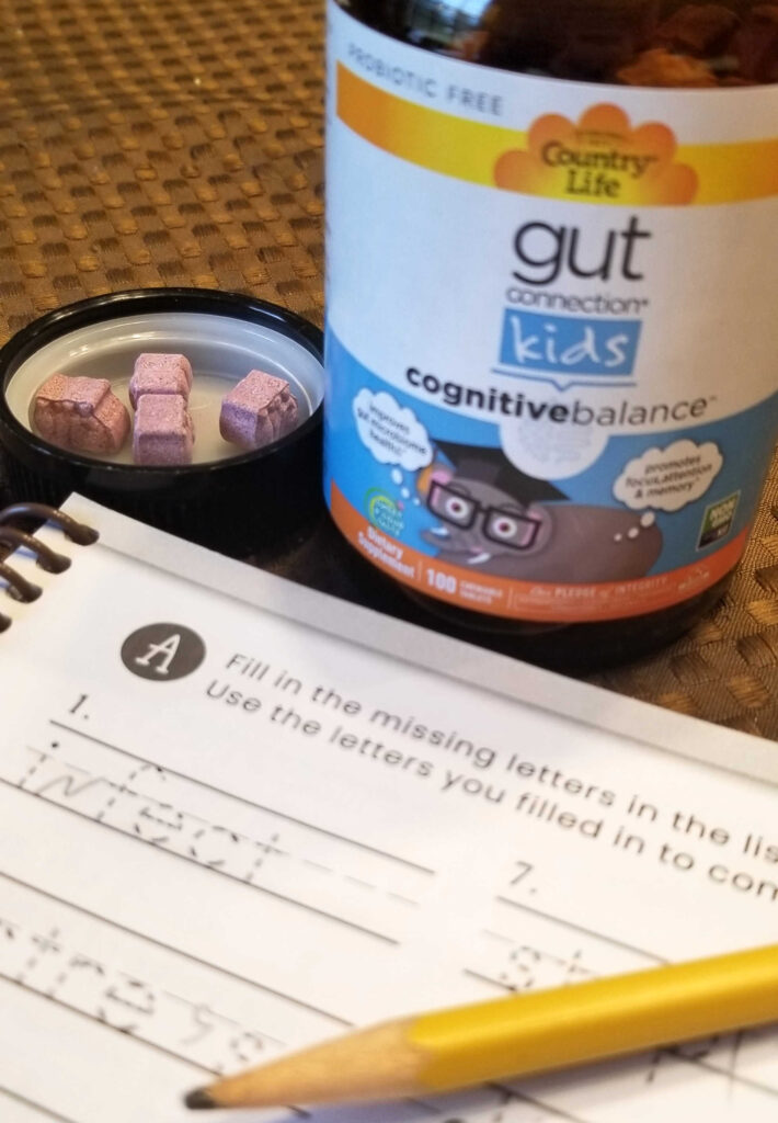 Gut Connection™ Kids Cognitive Balance™ chewable tablets alongside spelling workbook.