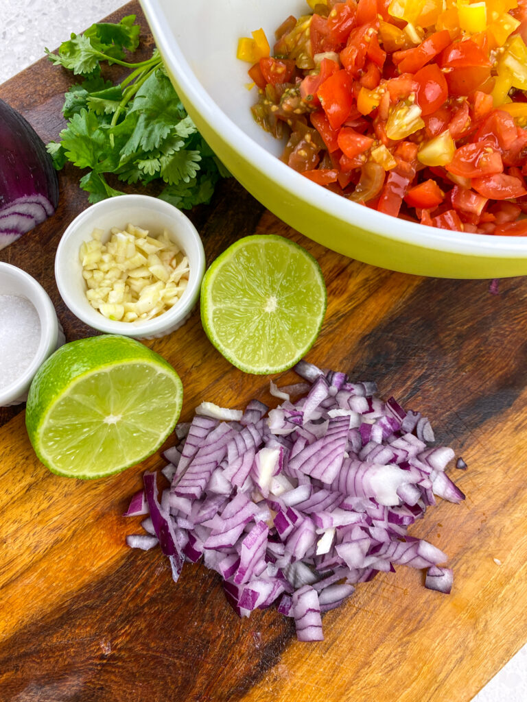 Diced red onion, garlic, tomatoes, cut lime and parsley on wood cutting board or in bowls.