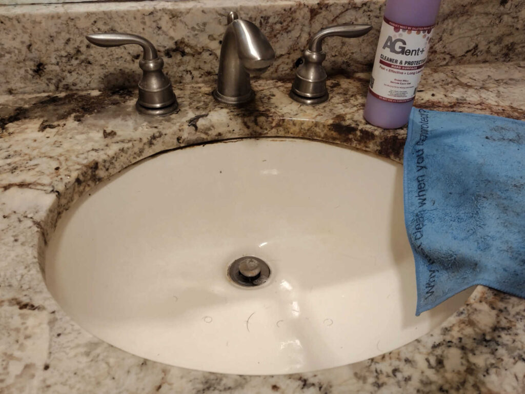 Bathroom sink with bottle of AGent+ Hard Surface Cleaner and Protectant next to used microfiber cloth.