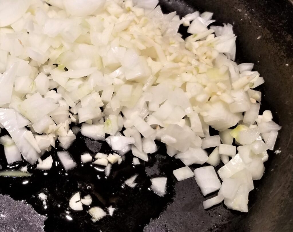 Diced onions are sauteed in cast iron pan with olive oil.