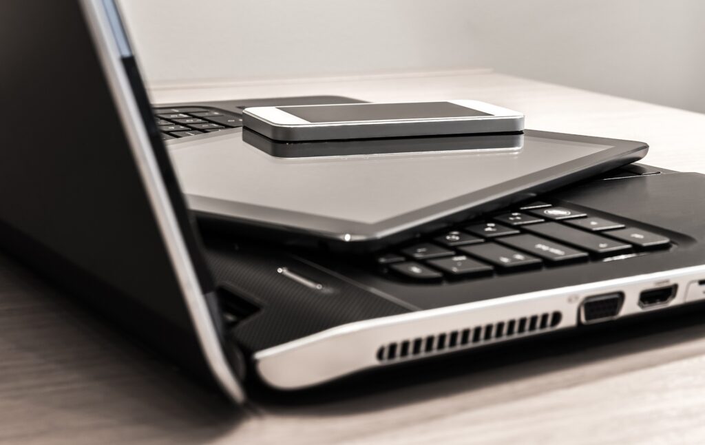 Cell phone and tablet sit on top of an open laptop.