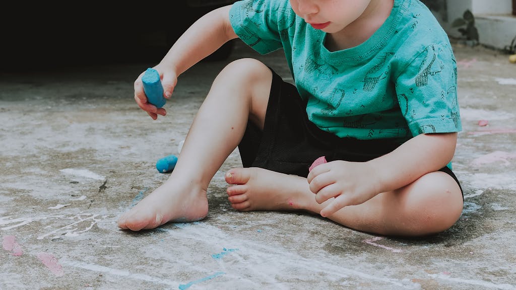 A young child sitting on the ground enjoying creative play with colorful chalk outdoors.