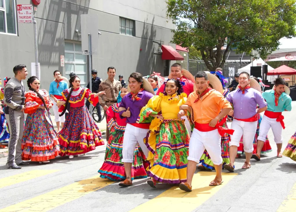 Men and women in colorful Mexican dress march down the road.