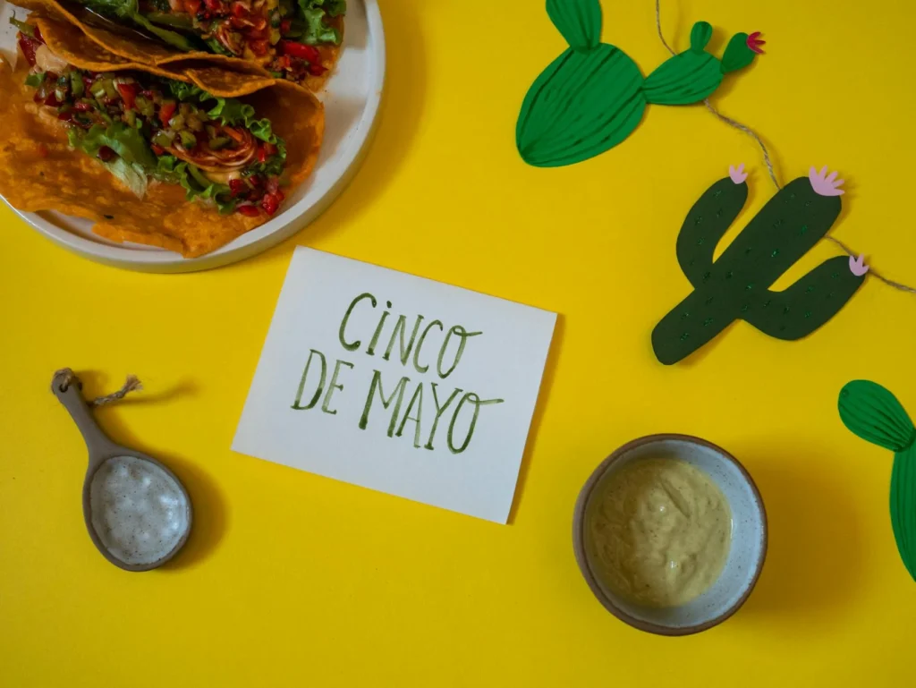Yellow table holds a dish of food, a string of cactus cutouts, and an index card with Cinco de Mayo written on it.