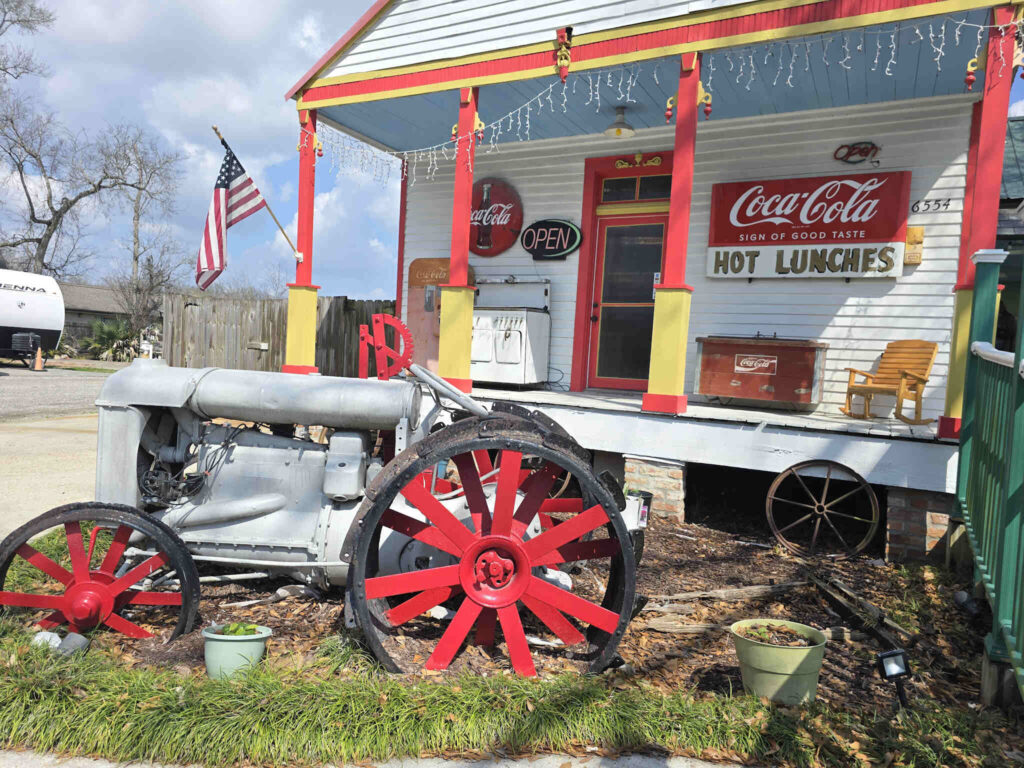 Historic roadside restaurant in Convent, Louisiana, featuring vintage Coca-Cola signs, a front porch with rocking chairs, and an antique tractor displayed in front of the building.