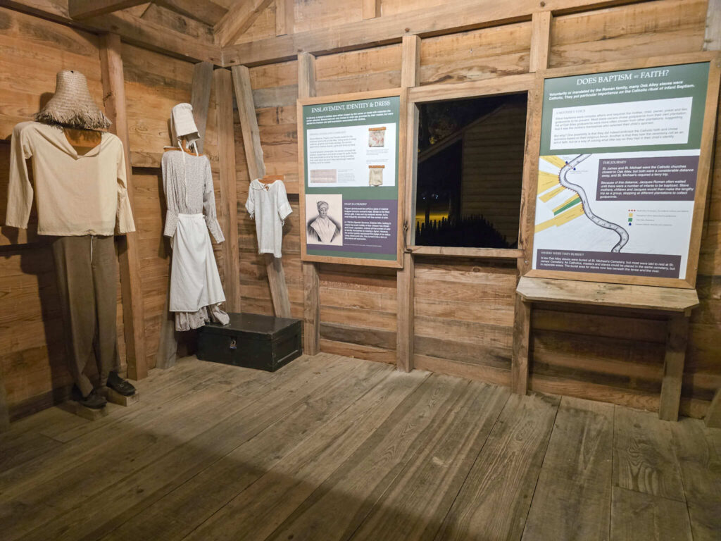 Interpretive exhibit inside a restored slave cabin at Oak Alley Plantation featuring historical information panels, period clothing displays, and exhibits about the lives of enslaved people.