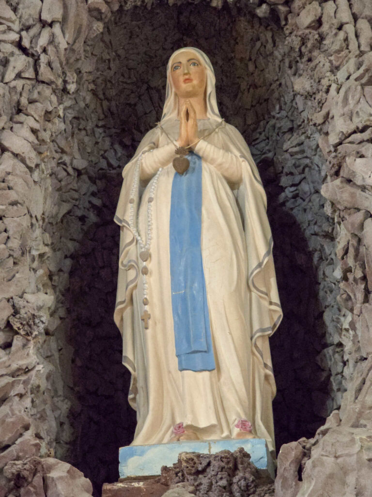 Statue of the Blessed Virgin Mary standing in prayer inside the Lourdes Grotto at St. Michael the Archangel Church in Convent, Louisiana.