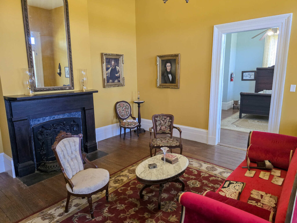Historic sitting room at St. Joseph Plantation with antique furniture, portraits, a marble-top table, and a black fireplace mantel.