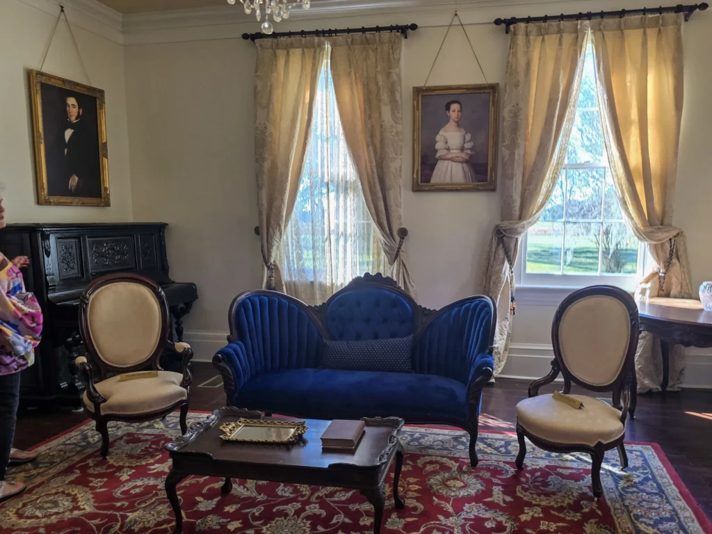 Elegant parlor room inside Felicity Plantation featuring antique furniture, portraits, tall windows, and historic decor.