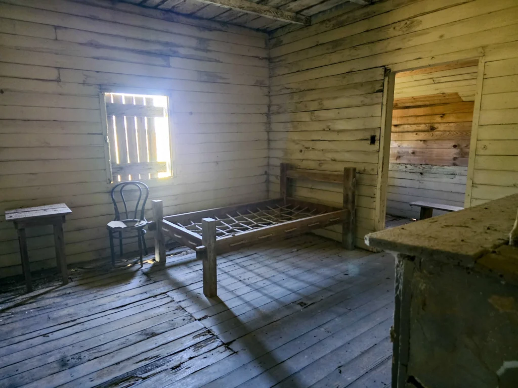 Interior of a preserved slave cabin at St. Joseph Plantation showing a simple wooden bed, walls, and living space.