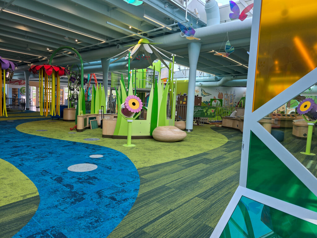Bright, colorful indoor play and learning area at the Children’s Museum of Richmond featuring oversized flowers, grass, and interactive exhibits.