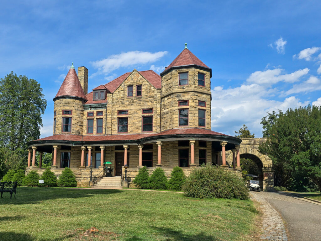 Stone Maymont Mansion in Richmond, Virginia, featuring turreted towers, red roofs, a wraparound porch, and landscaped grounds.