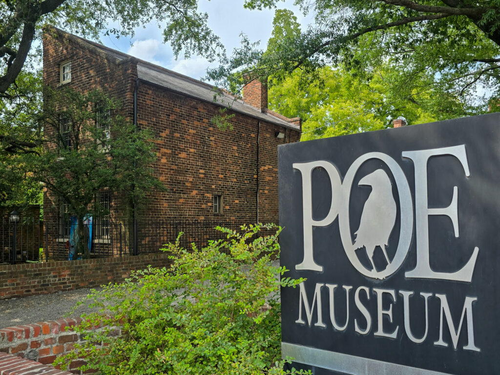 Poe Museum sign in front of the historic brick Old Stone House surrounded by leafy trees in Richmond, Virginia.