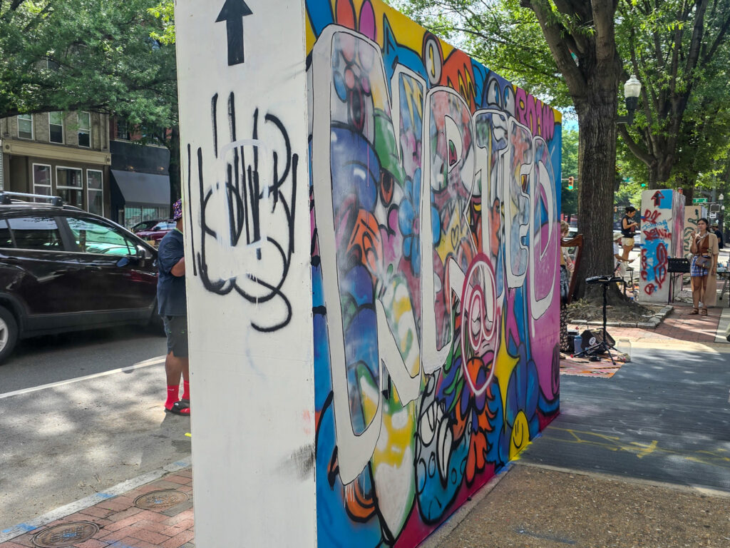 Colorful pop-up mural covered with graffiti-style artwork during an arts event in Richmond, Virginia, with a musician performing nearby.