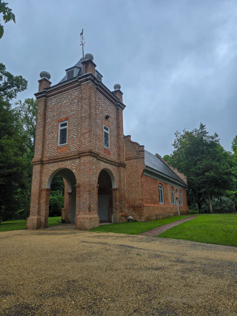 Historic brick St. Peter’s Church in Virginia with a tall square bell tower, arched entryways, and surrounding trees.